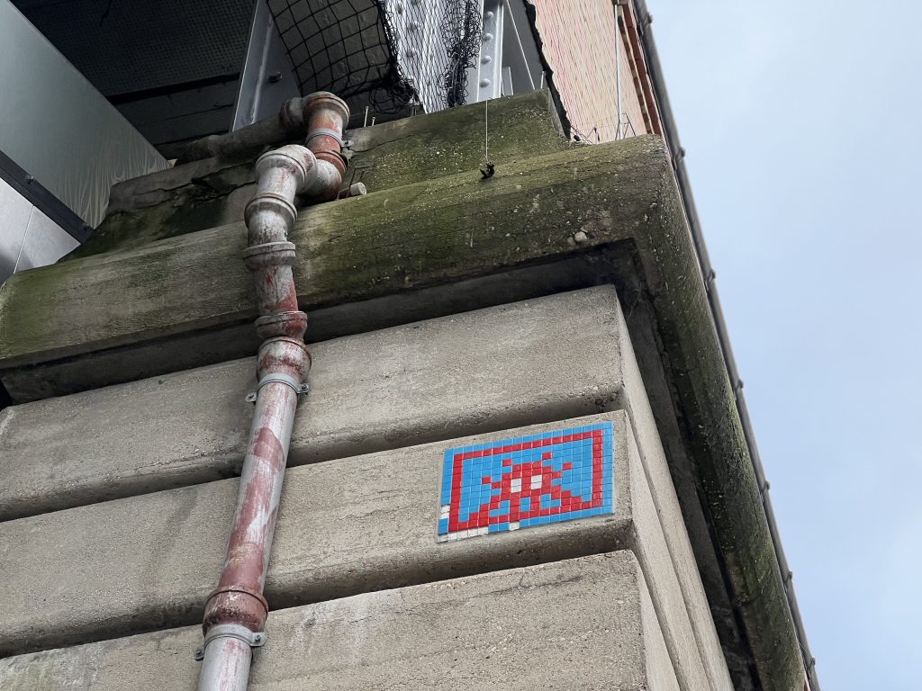 Invader mosaic pixel art on the sky train bridge near Place du Dupleix, Paris, adding a touch of urban artistry to the metallic structure against the cityscape.